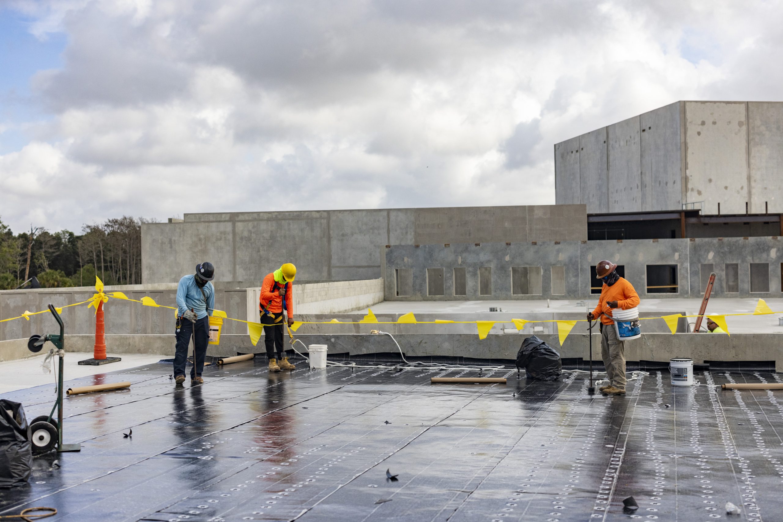CFS Roofing crew laying flat-roof base sheet at the Greater Good school project